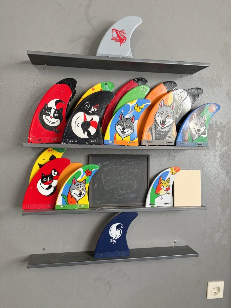 Pranchas de surf apoiadas em suportes de madeira contra parede branca, com iluminação pendente.