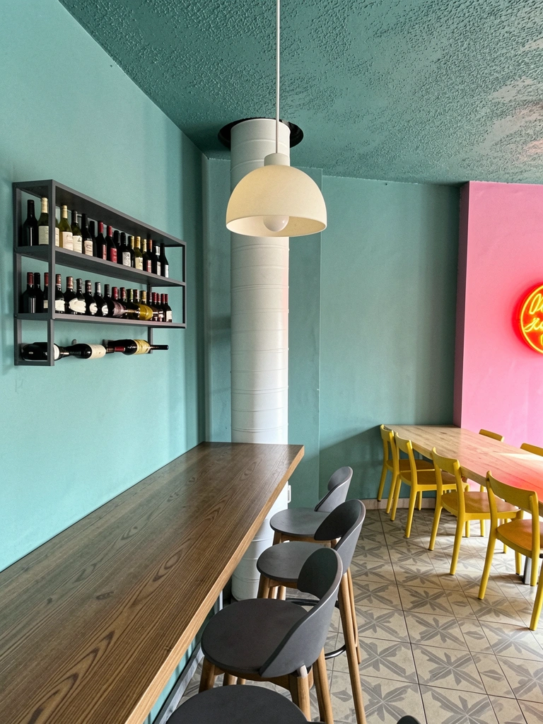 Ambiente interno de wine bar com balcão de madeira, banquetas altas e prateleiras de garrafas sob luz âmbar.